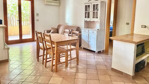 A room with a dining table, chairs, a sofa, a cabinet, and a kitchenette. - Villino Marzamemi (Marzamemi)