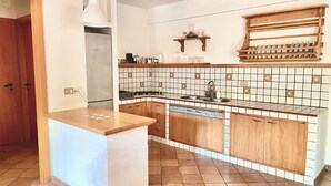 A kitchen with wooden cabinets, a tiled backsplash, a built-in oven, and a wooden shelf above the sink. - Villino Marzamemi (Marzamemi)