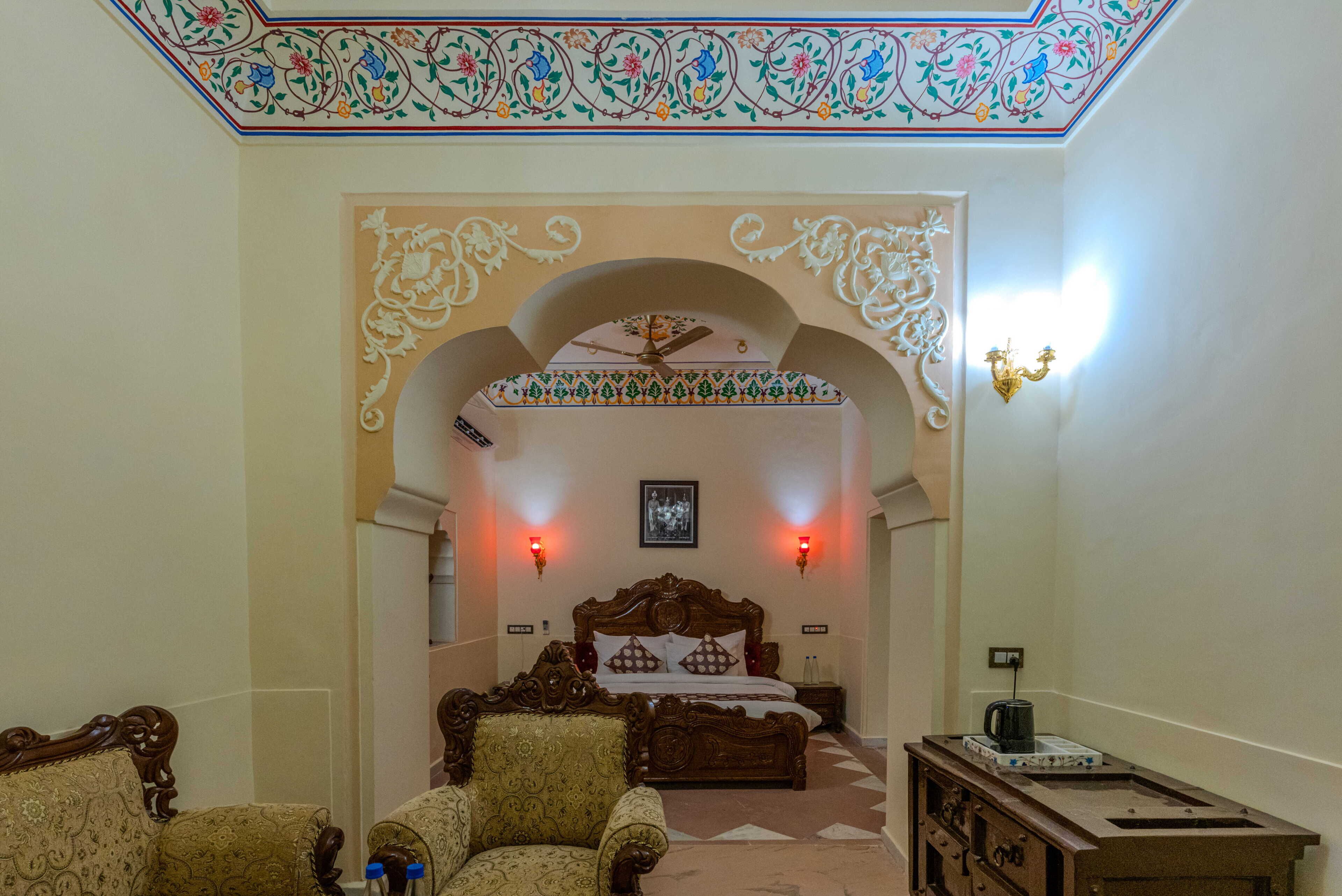 A hotel room with a bed, two chairs, a nightstand, and a decorative ceiling.