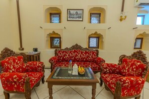 A traditional room with a sofa set, a table with a bottle and fruit, and decorative wall panels.