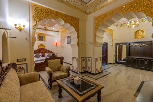 A traditional room with ornate decor, a bed, seating area, and a mirror.