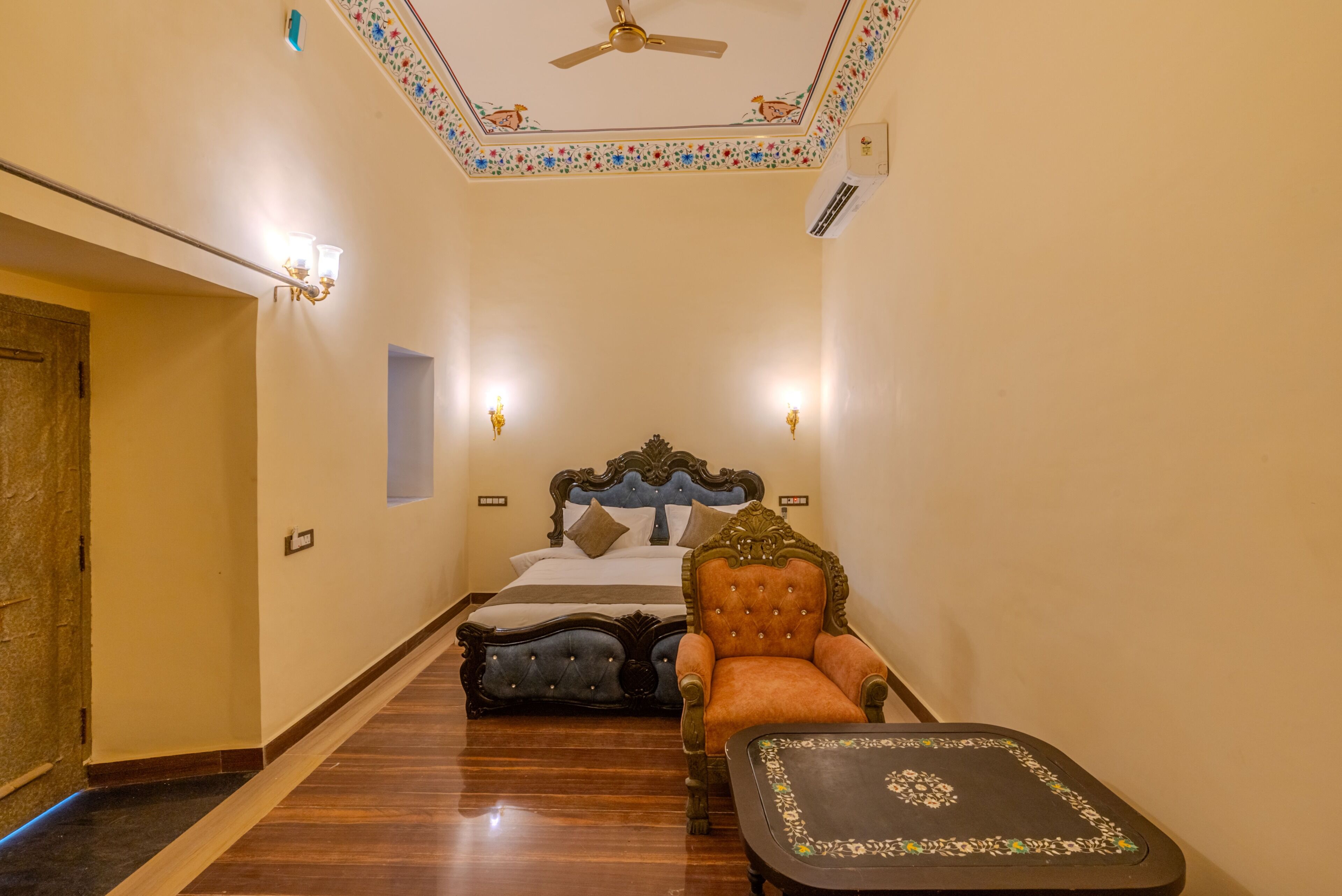 Een hotelkamer met een bed, een stoel, een tafel, een plafondventilator en decoratieve wandpanelen.