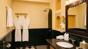 A bathroom with a checkered floor, a toilet, a sink with a mirror, and two white robes hanging on a rack.