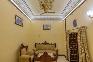 A room with a ceiling fan, a sofa, a table, and a door with a patterned curtain. - Mahal Khas Palace (Bharatpur)