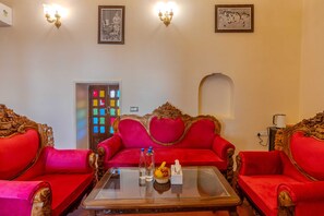 A room with a red upholstered sofa, a glass coffee table, and ornate wooden furniture.