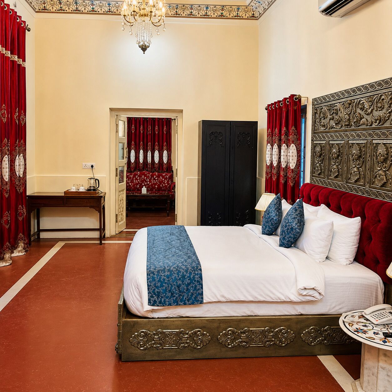 A hotel room with a large bed, a desk, a wardrobe, and a chandelier.