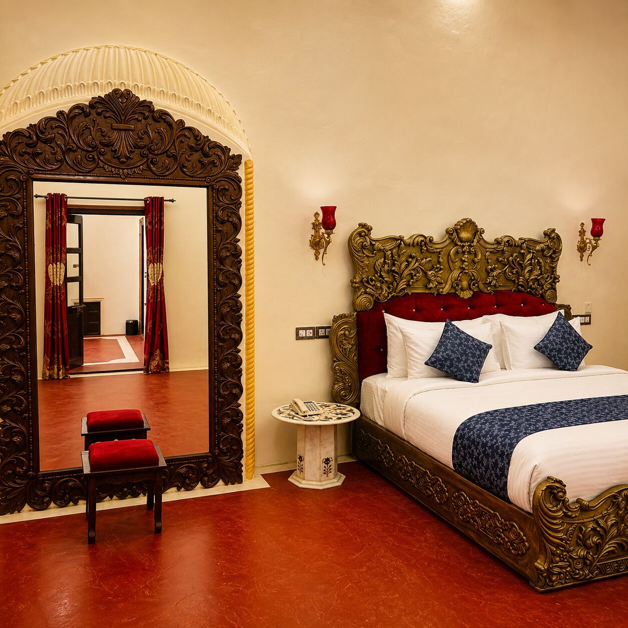 A room with a large ornate mirror, a bed with red and blue bedding, and a small table with a telephone.