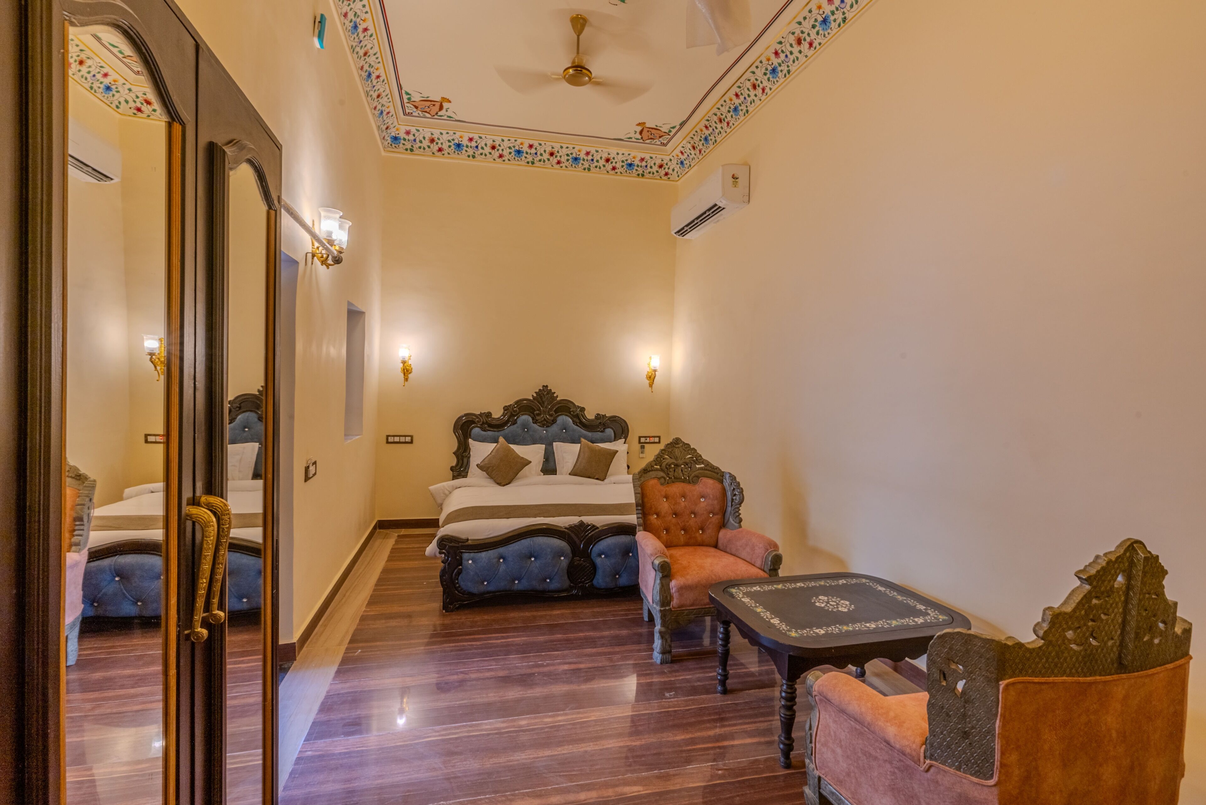 A hotel room with a large bed, a chair, a small table, and a mirror.