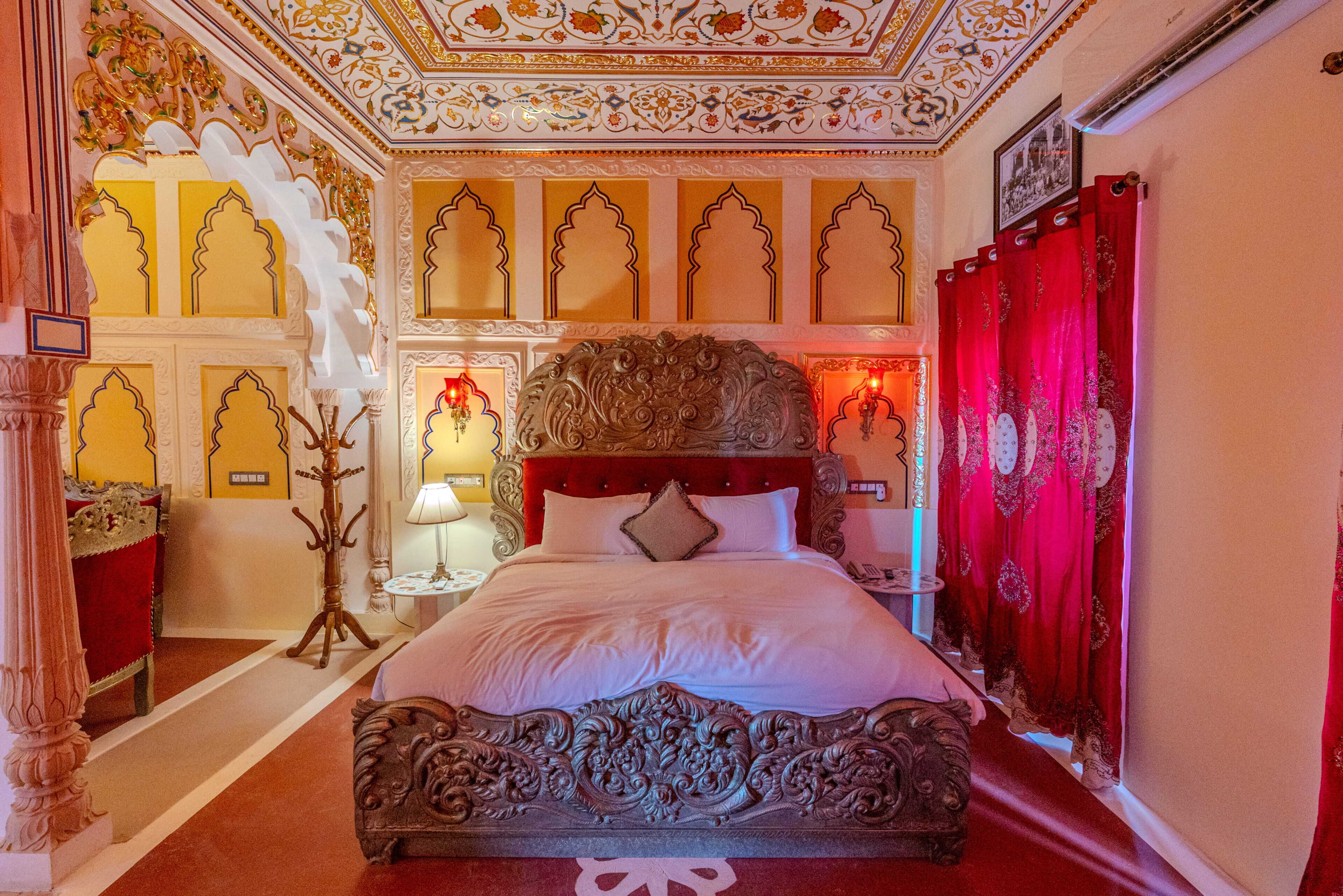A room with a large bed, ornate ceiling, and red curtains.