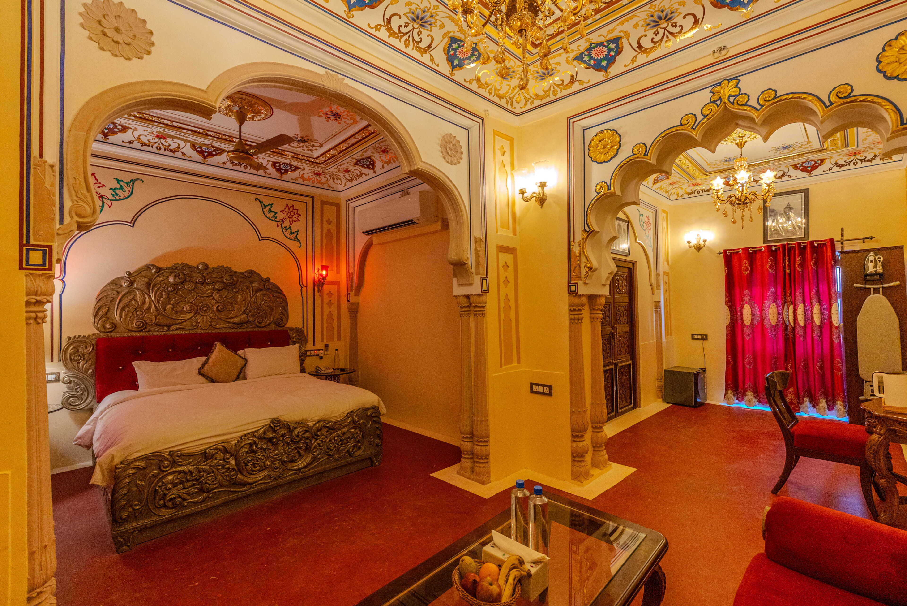 Una habitación lujosa con una cama ornamentada, un sofá rojo y una araña.