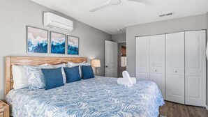 A bedroom with a bed, a ceiling fan, an air conditioning unit, and a wardrobe. - Sea Salt & Sunny Days: Pool, Spa, Putting Green by Anna Maria Life Vacation Rentals (Holmes Beach)