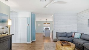 A modern living room with a gray sofa, a wooden coffee table, and a view of a kitchen area. - Sea Salt & Sunny Days: Pool, Spa, Putting Green by Anna Maria Life Vacation Rentals (Holmes Beach)