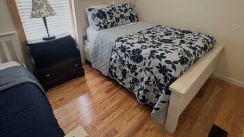 Un dormitorio con cama, mesita de noche, lámpara y ventana con persianas.