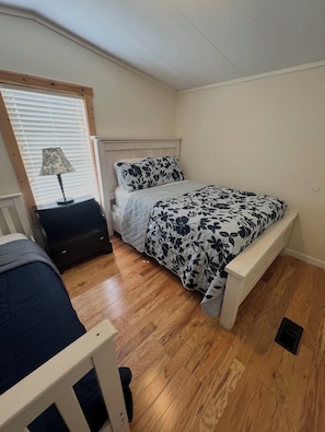 A bedroom with a bed, a nightstand, a lamp, and a window with blinds.
