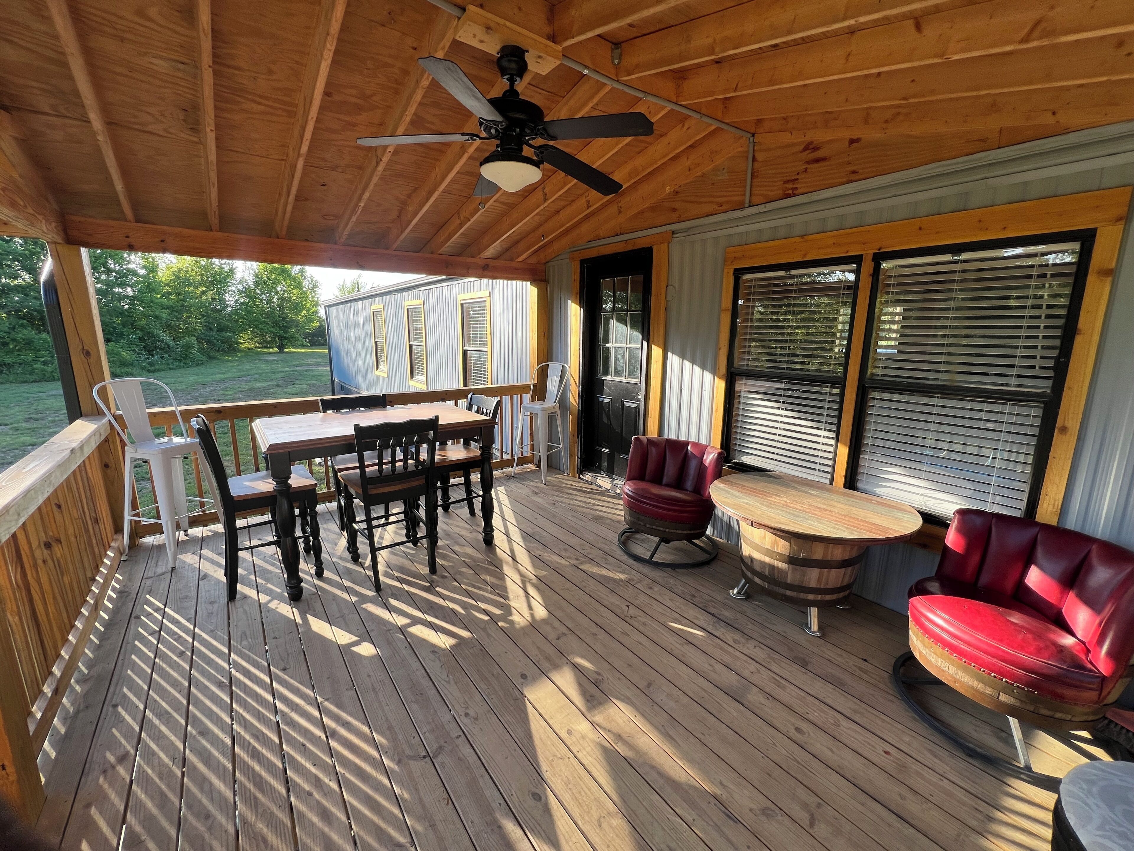 A covered deck with a wooden table and chairs, a ceiling fan, and a view of a blue house.