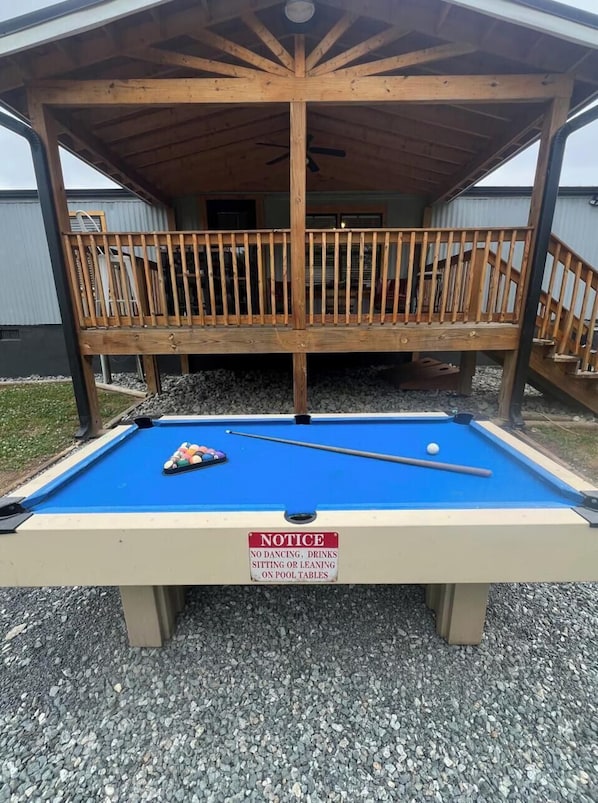 A pool table with a notice sign, a wooden deck, and a building in the background.