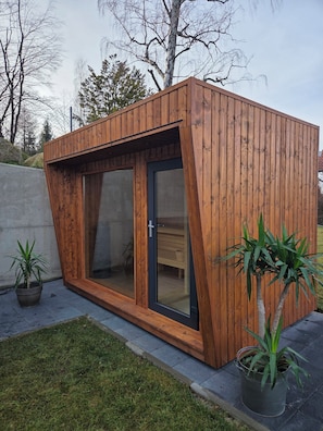 Eine moderne Holzkonstruktion mit großen Glasüren, einer Betonwand und einem Grünbereich mit Topfpflanzen.