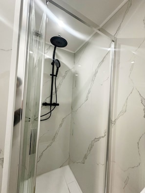Un box de ducha moderno con puerta de vidrio, paredes de mármol y cabezal de ducha de mano.