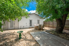 A white building with a patio, a table and chairs, and a tree.