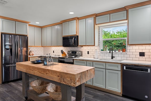 A modern kitchen with light grey cabinets, stainless steel appliances, and a wooden island.