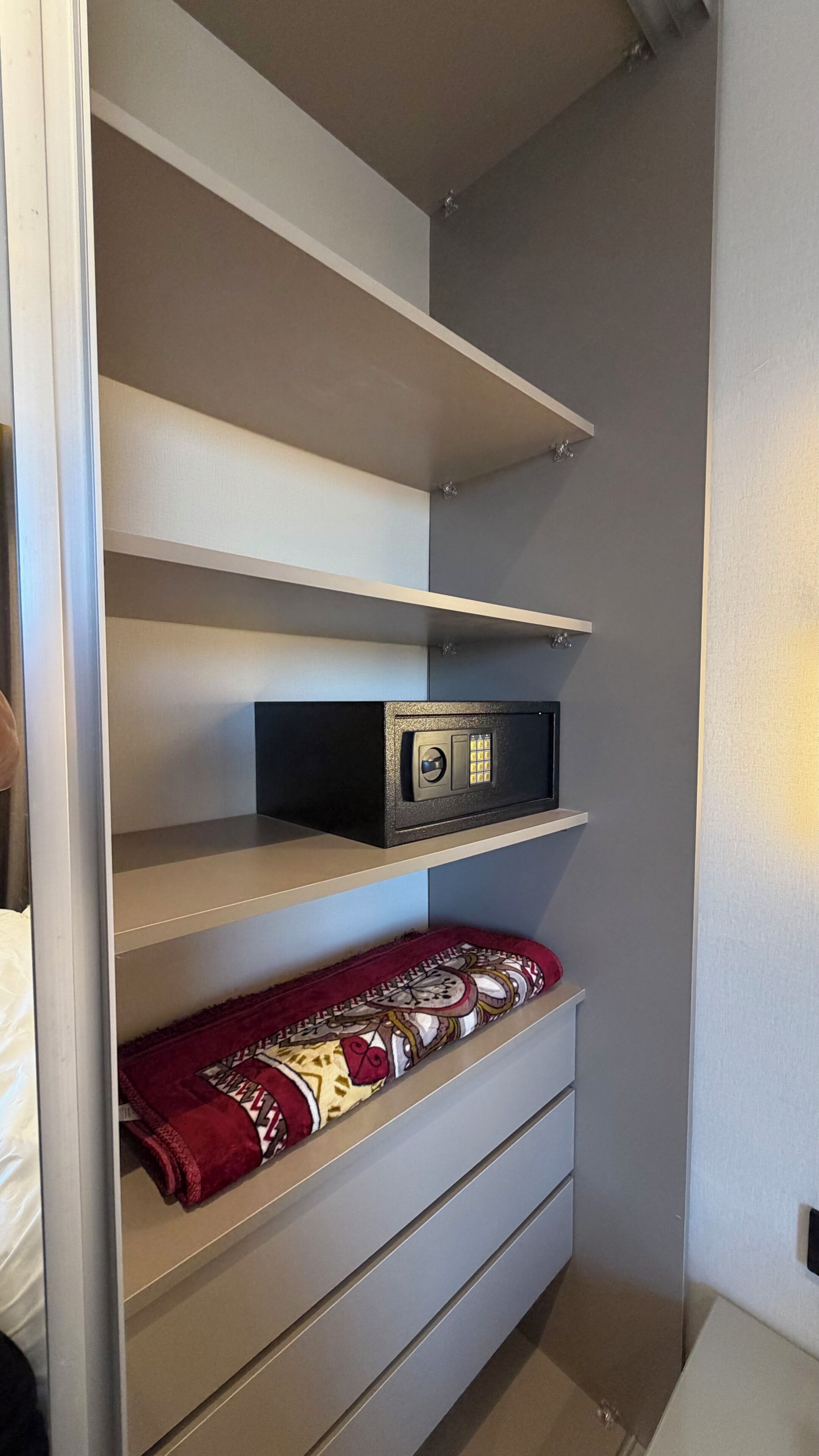 Un espace de rangement comprenant un coffre-fort, une couverture à motifs et un lit.