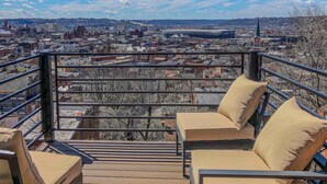 A balcony with a city view, a railing, and two beige cushioned chairs. - City View Perch Walkable Apt (Cincinnati)