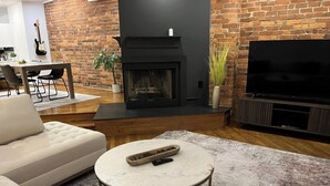 A living room with a fireplace, a sofa, a coffee table, and a TV. - City View Perch Walkable Apt (Cincinnati)