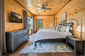 Ein Schlafzimmer einer Holzhütte mit Bett, Schminktisch, Nachttisch und Deckenventilator.