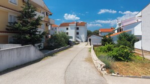 Un carrer estret flanquejat per edificis residencials amb balcons, un cotxe aparcat i un cel blau clar.