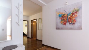 Un passadís amb terra de fusta, una paret blanca amb un quadre de papallona i una porta que condueix a una altra habitació.