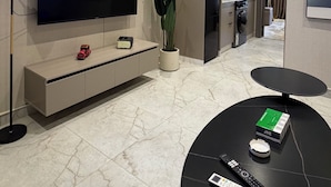 Een moderne woonkamer met een flatscreen televisie, een potplant, een salontafel en een keuken op de achtergrond.