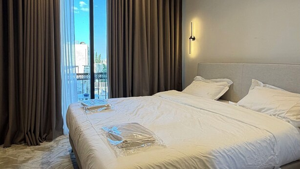 Een moderne hotelkamer met een groot bed, stadszicht en een balkon met gordijnen.