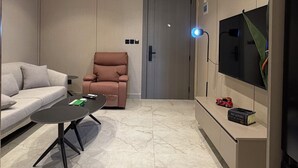 Een moderne woonkamer met een bank, een fauteuil, een salontafel, een aan de muur bevestigde televisie en inbouwspots.