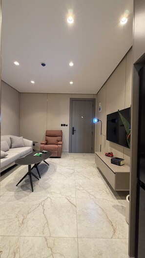 A modern living room with a sofa, a recliner, a coffee table, a TV mounted on the wall, and recessed ceiling lights. - 303 Tara-jre Jabal Al Lweibdeh With Stunning View (Amman)