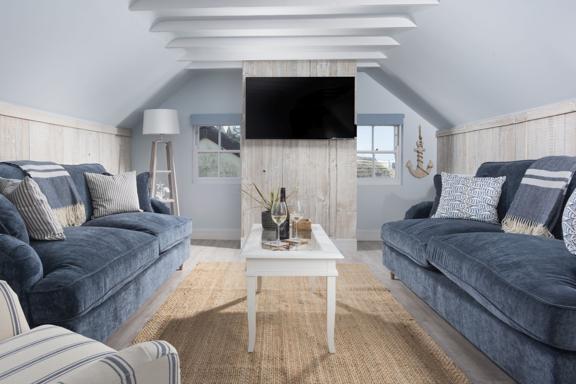 A modern living room with two sofas, a coffee table, a flat-screen TV mounted on the ceiling, and a view of the outdoors.