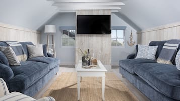 A modern living room with two sofas, a coffee table, a flat-screen TV mounted on the ceiling, and a view of the outdoors.