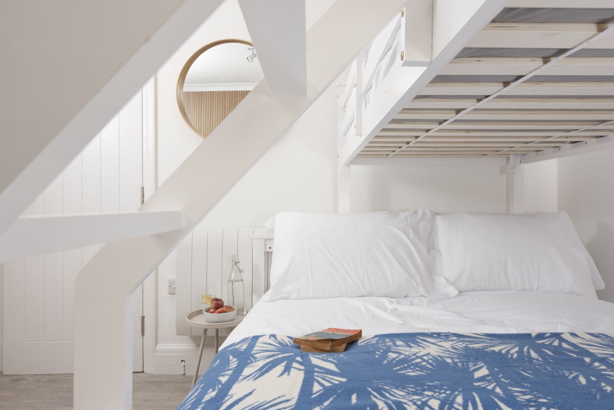 A bedroom with a bunk bed, a round mirror, a small table with fruit, and a patterned bedspread.