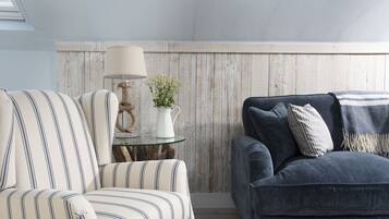 A living room with striped armchairs, a dark sofa, a glass coffee table with a lamp and a plant, and a wooden wall.