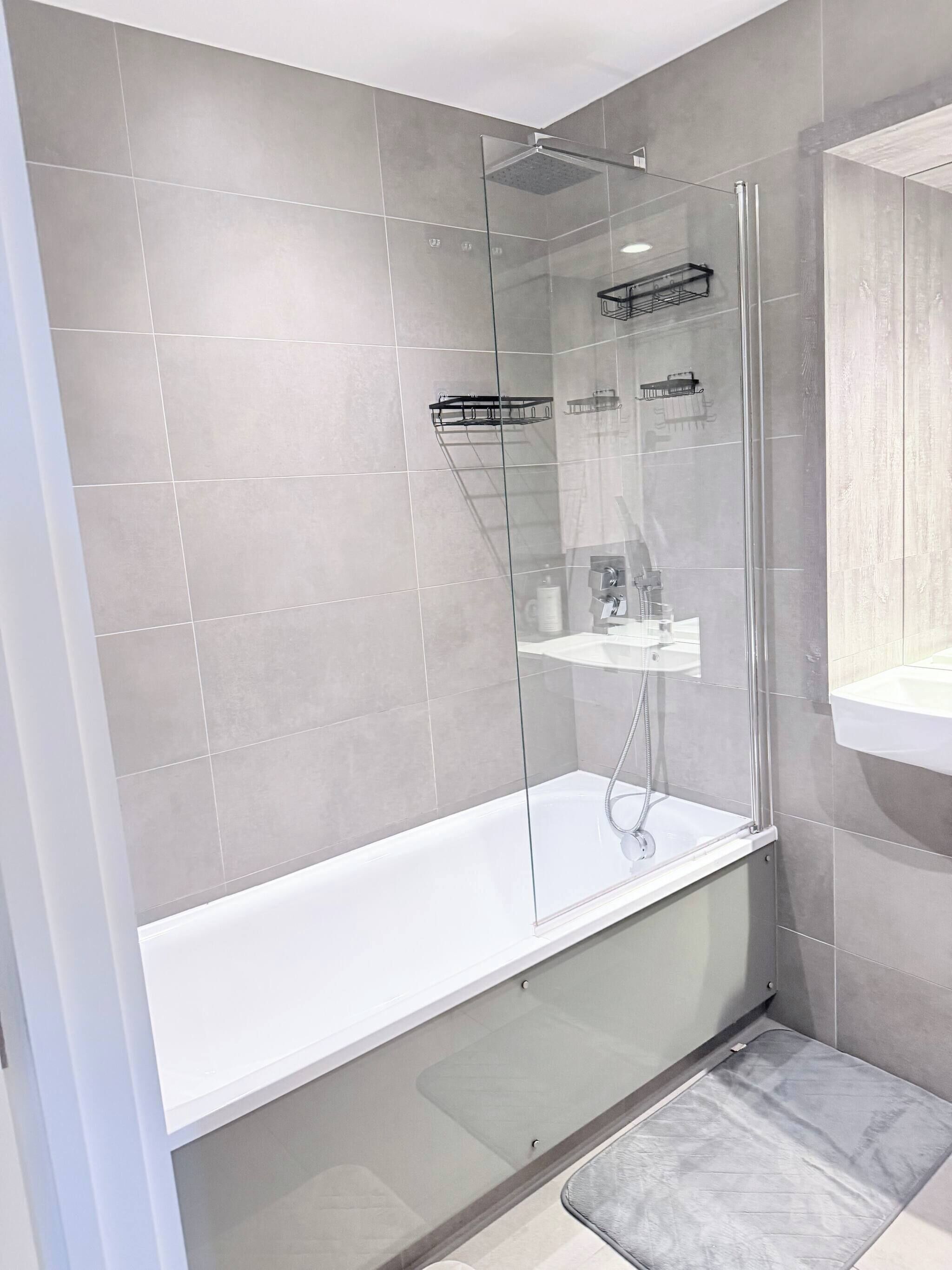 Une salle de bain moderne avec une douche à parois de verre, une baignoire blanche et un mur recouvert de carreaux gris.