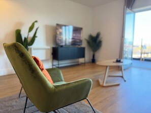 A modern living room with a green armchair, a small round table, and a TV on a stand. - Charming Cozy One-bedroom Apartment With Ps5 (Birmingham)