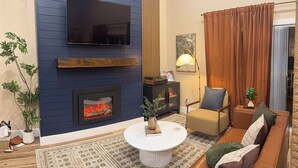 Ein Wohnzimmer mit Kamin, Wandfernseher, Sofa, Couchtisch und Lampe.