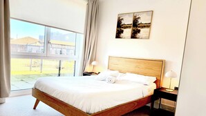 Una camera d'albergo con un letto grande, un comodino con una lampada, una finestra con vista esterna e due quadri appesi al muro.