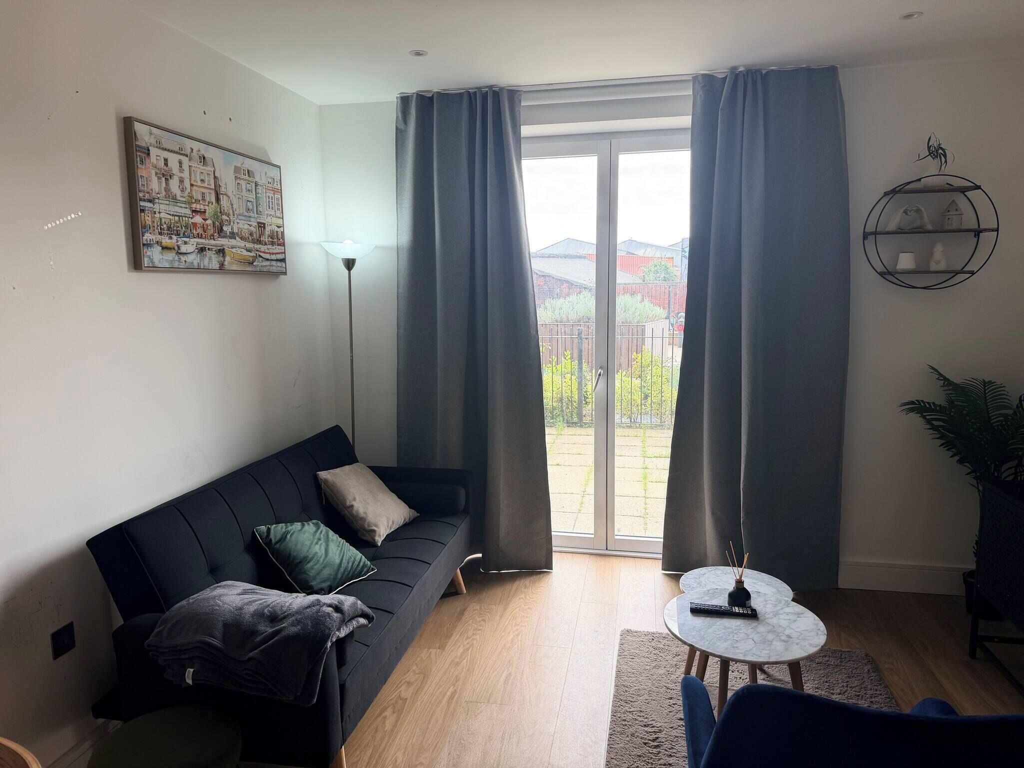 A modern living room with a black sofa, a small round table, and a large window with curtains.