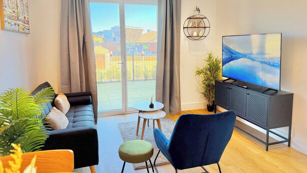 Un soggiorno moderno con divano, una poltrona blu, televisione e un balcone con vista.