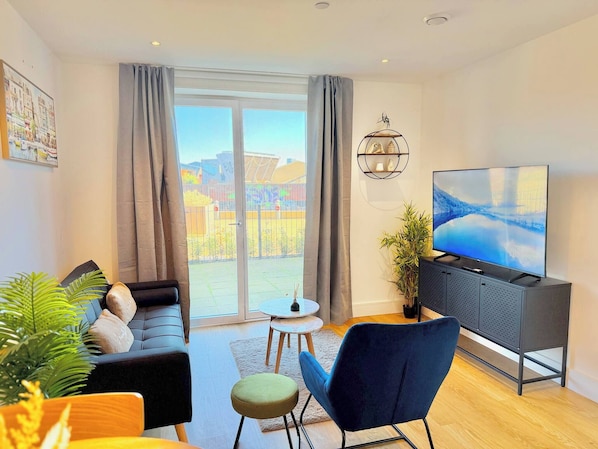 A modern living room with a sofa, a blue chair, a TV, and a balcony with a view. - One Bedroom West Midlands Retreat (Birmingham)