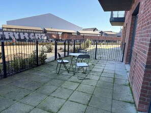 A courtyard with a paved patio, two folding chairs, a metal table, and a brick building in the background. - One Bedroom West Midlands Retreat (Birmingham)