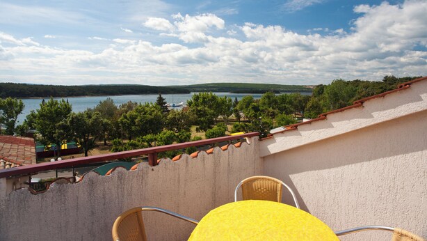 Un balcon donnant sur un lac, des arbres et des collines lointaines.