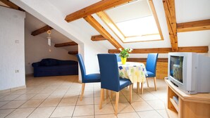 Une pièce avec un plafond en pente, des poutres en bois, un canapé, des fauteuils, une table avec une plante et un téléviseur.