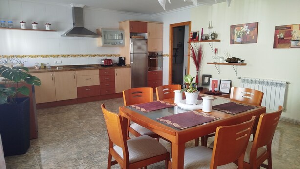 A dining area with a wooden table and chairs, a kitchen in the background, and a radiator on the wall. - APARTMENT FOR CYCLISTS IN BENISSA, COSTA BLANCA (Benissa)