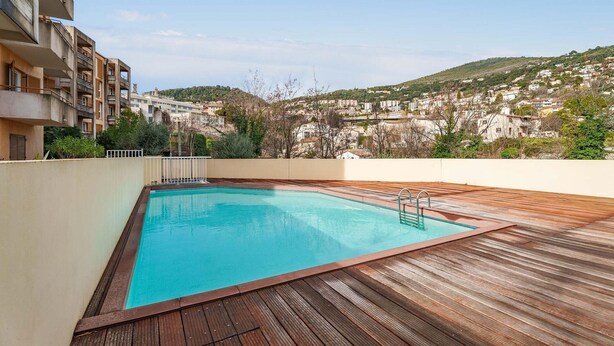 A rooftop swimming pool with a wooden deck, surrounded by buildings and a hillside in the background. - Scenic Riviera Home Near sea (Grasse)